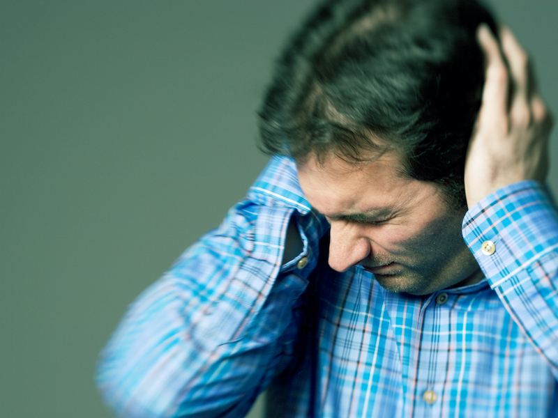 Man troubled by bothersome noises holding hands over his ears to block them out.