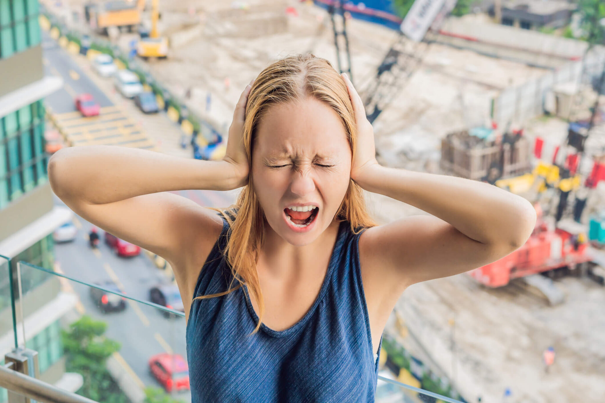 A young woman by the window bothered by the loud construction work outside.