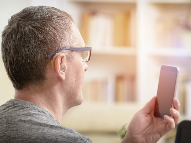 Hearing impaired man working with laptop and mobile phone at home or office while wearing hearing aids and glasses at the same time.
