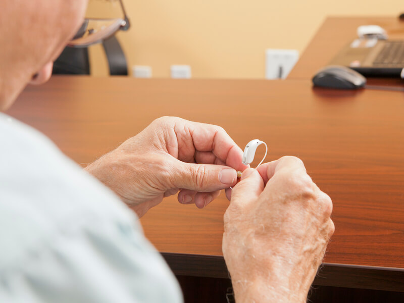 A gentleman troubleshooting what could be wrong with his hearing aid while sitting at his desk.