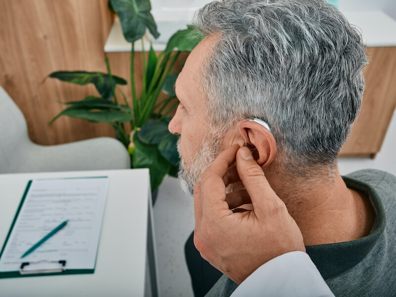 Hearing Aid Specialist fits a hearing aid on mature man ear while visit a hearing clinic.
