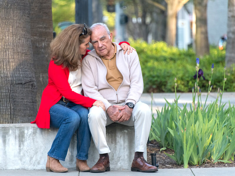 Woman embracing man with hearing loss in park because he is feeling depressed.