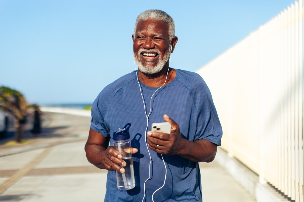 man runs along a seaside promenade holding a water bottle and smartphone.