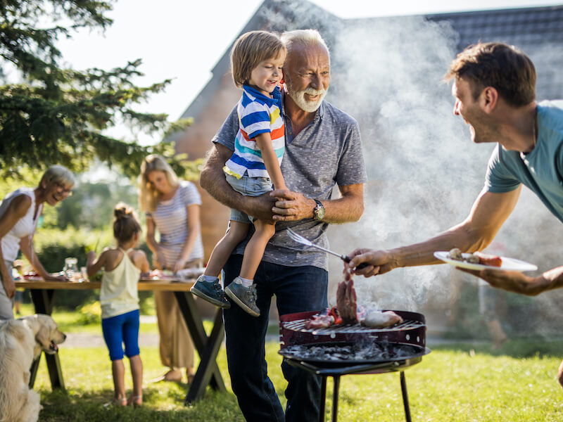 Man holding grandson at family cookout waiting for grilled food to be done 