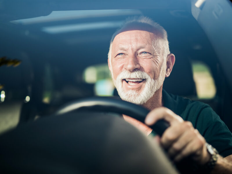 Older man behind the wheel of his car excited to drive since he solved his hearing loss.